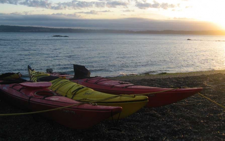 a group of kayaks rest on the shore of a vast body of water in the pacific northwest